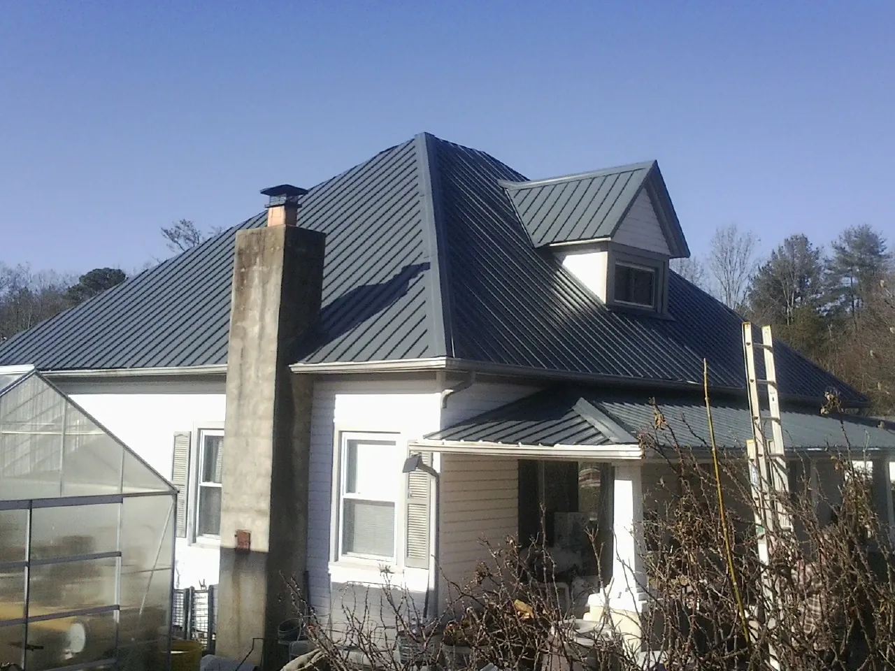 Dark blue standing seam metal roof on a white farmhouse with dormer — Slate & Tile Roof Repair by Roofing Brothers in Westover