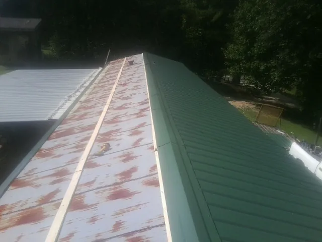 Old rusted panels beside newly installed green metal roofing — Wind Damage Roof Repair by Roofing Brothers in Westover