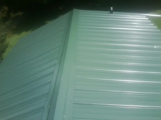New green metal panels meeting at the ridge of a roof — Flat Roof Repair work by our crew in Westover