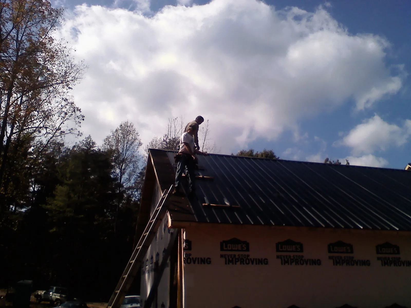 Roofer fastening dark metal panels high against a cloudy sky, from a Roof Inspection job in Westover